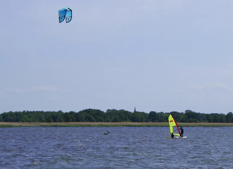 Windsurfer i latawiec kitesurfera nad jeziorem Resko Przymorskie, w tle las na brzegu
