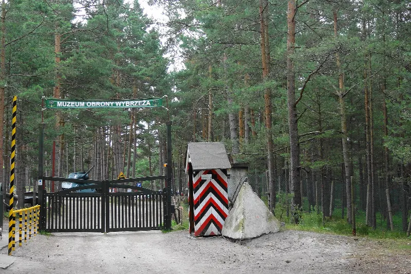 Brama wjazdowa Muzeum Obrony Wybrzeża w Helu z biało-czerwonym szlabanem i budką wartowniczą