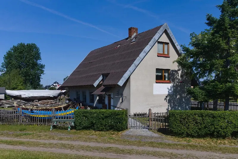 Dom Muzeum Rybackiego Pod Strzechą w Jastarni ze stromym dachem i łodziami przy płocie