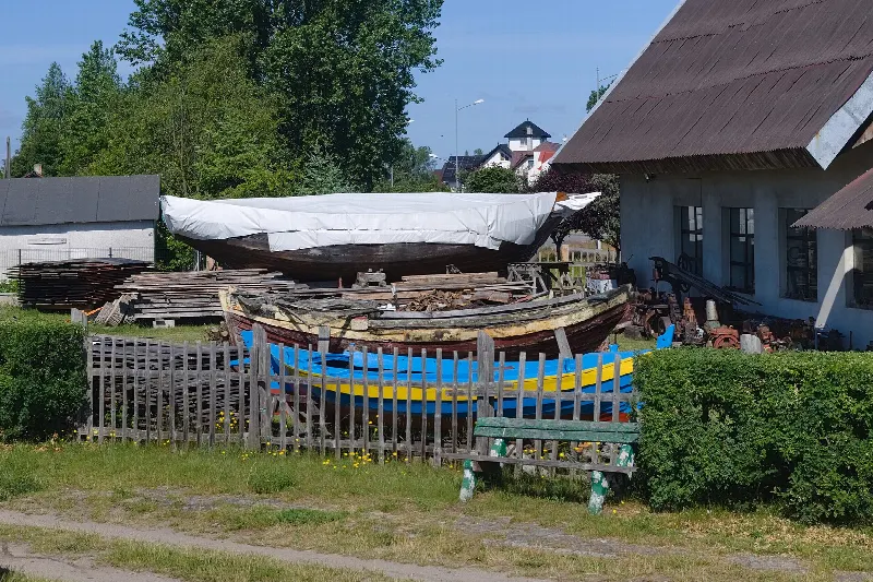 Drewniane łodzie i deski przed warsztatem szkutniczym Muzeum Pod Strzechą w Jastarni