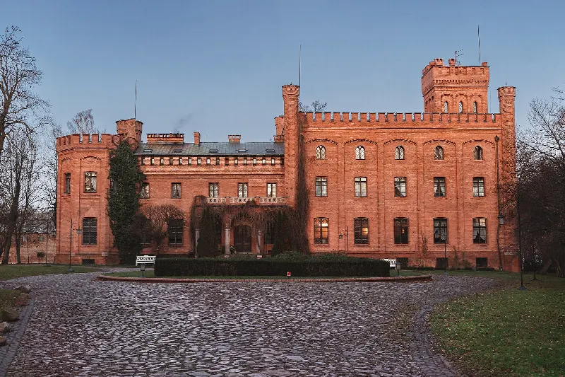 Neogotycki pałac w Rzucewie z ceglanymi wieżami i krenelażem, widok od strony brukowanego podjazdu