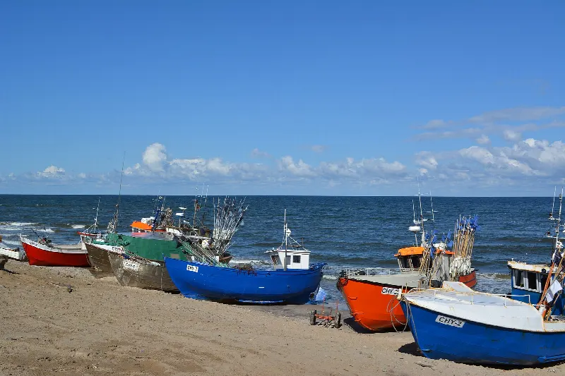Kolorowe łodzie rybackie wyciągnięte na plażę przy przystani w Chłopach, za nimi morze